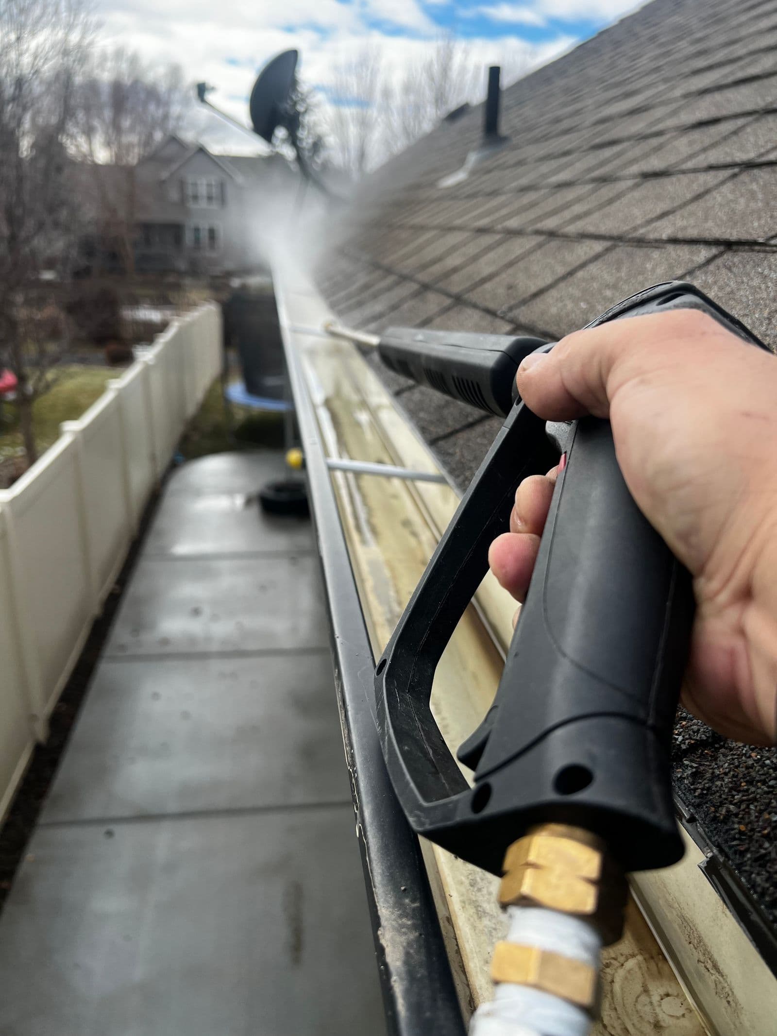 A technician using a pressure washer to flush debris from a home's roof gutter